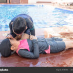 Boy helping drowning child girl in swimming pool by doing CPR.