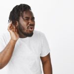 questioned-guy-with-braids-posing-against-white-wall_176420-29415